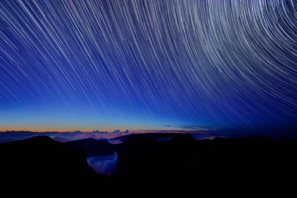 a star trail is seen in the sky above mountains
